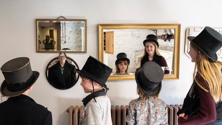 Several children trying on hats and looking at themselves in mirrors on the wall